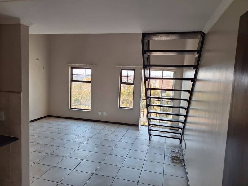 An open-plan living area featuring tiled flooring, large windows for natural light, and a modern metal staircase leading to an upper level.