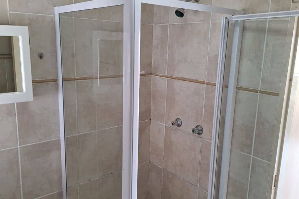 A functional bathroom featuring a corner shower enclosure with tiled walls and flooring, providing a clean and practical space.
