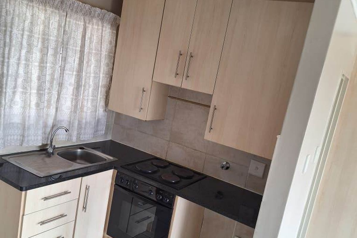 Compact kitchen featuring light wood-tone cabinetry, built-in oven, electric hob, and tiled flooring. The space is functional but would benefit from cosmetic updates.