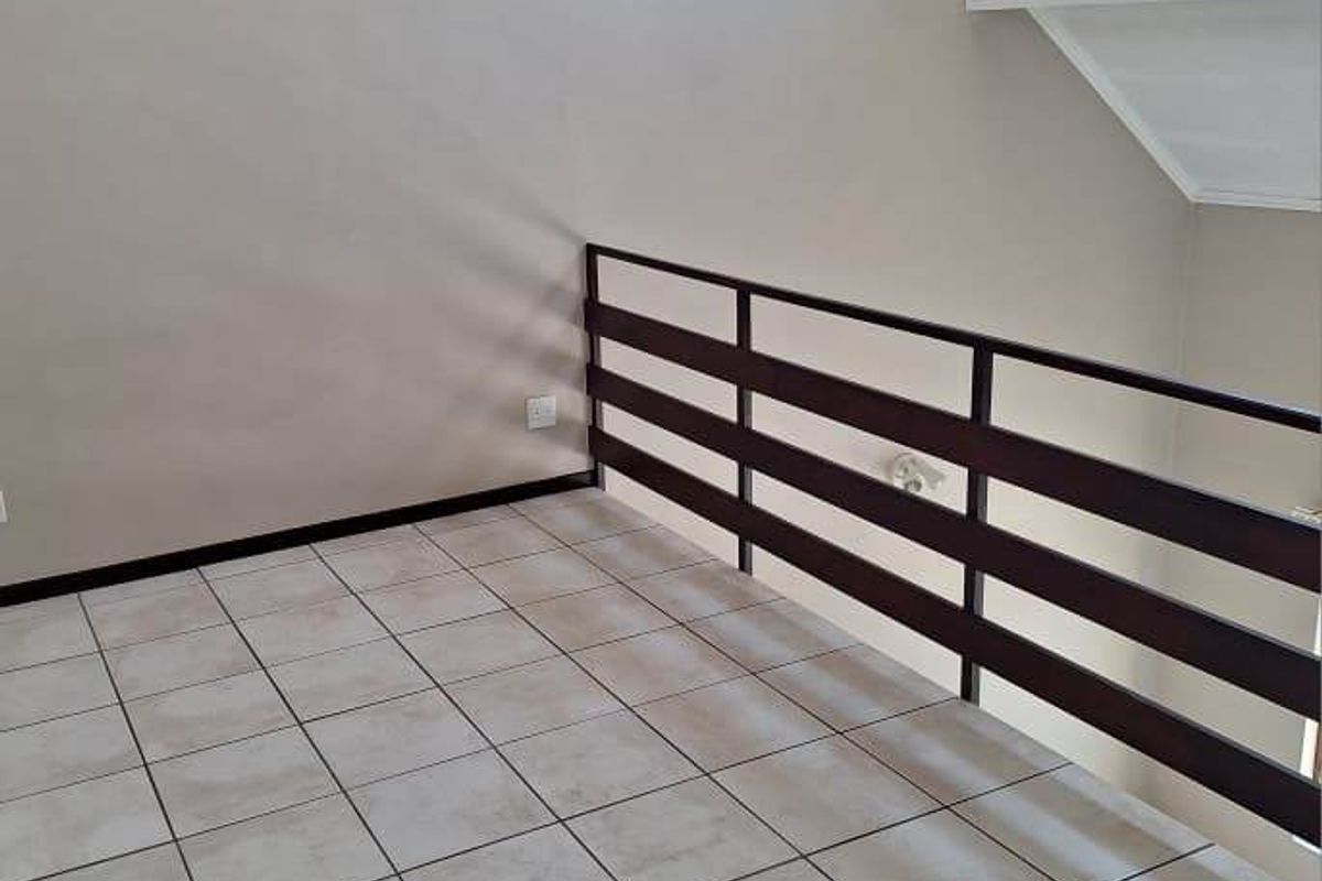 An empty loft-style bedroom area featuring tiled flooring, a metal safety balustrade, and a vaulted ceiling with a skylight.
