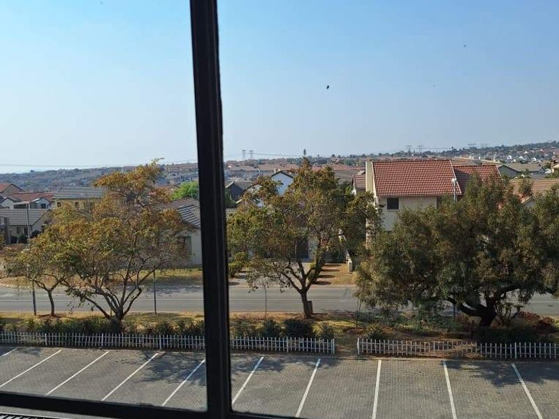 Elevated view from an apartment balcony overlooking a parking area, street, and surrounding residential neighborhood.