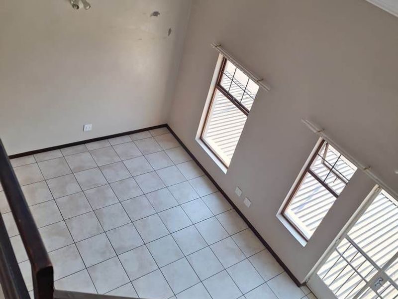 An empty, light-filled living area featuring tiled floors, a vaulted ceiling, and a metal staircase railing, viewed from an elevated position.