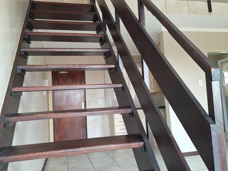 An open-plan interior space featuring a wooden staircase with a matching balustrade and tiled flooring throughout.
