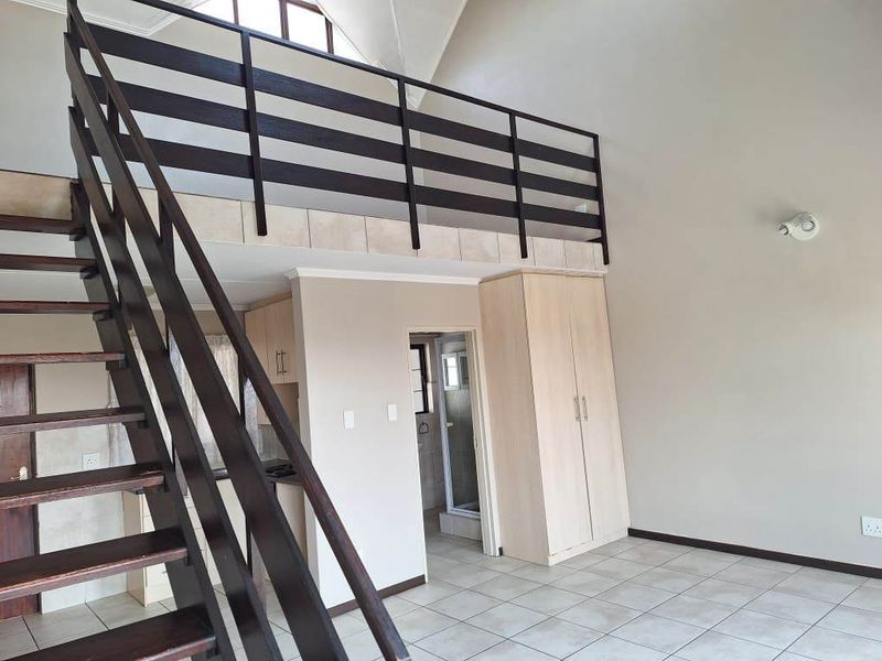 Open plan living area featuring a mezzanine level, timber staircase with balustrade, built-in storage, and tiled flooring under a vaulted ceiling.
