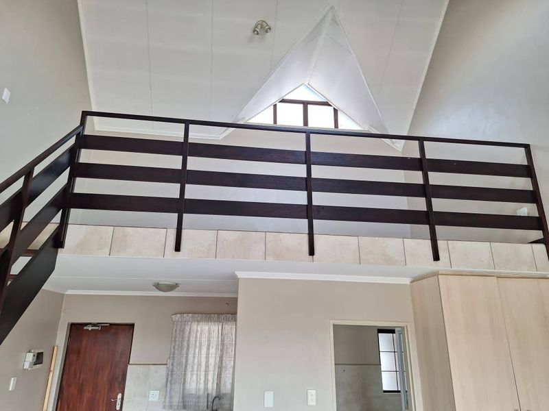 Open plan living area featuring a mezzanine level with timber balustrade, vaulted ceilings, and a unique triangular window providing natural light.