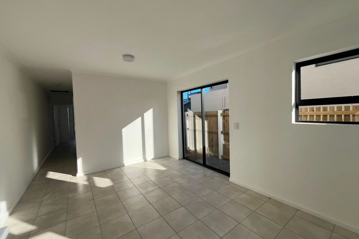 A bright, empty living area featuring neutral tiled flooring, modern black-framed windows, and a sliding glass door providing access to the exterior.
