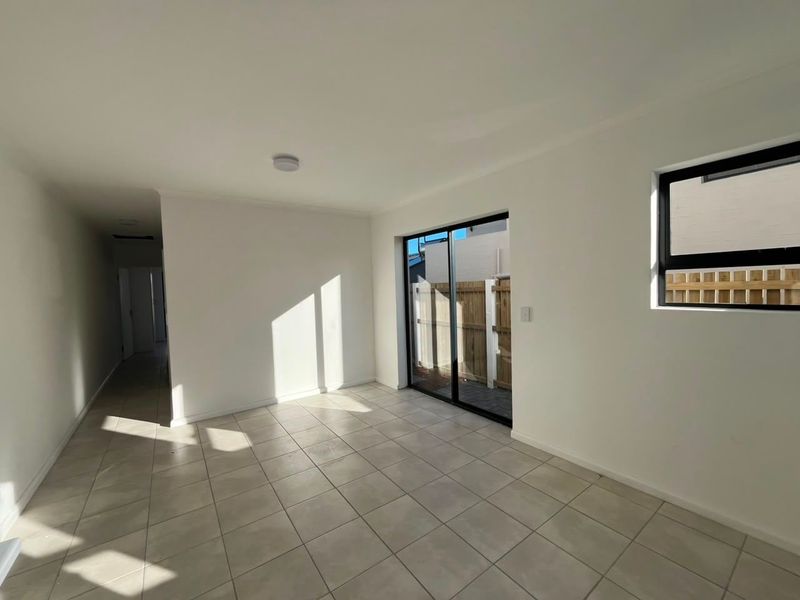 A bright, empty living area featuring neutral tiled flooring, modern black-framed windows, and a sliding glass door providing access to the exterior.