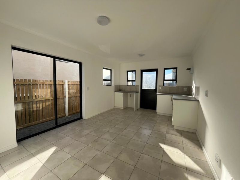 An open-plan kitchen and living area featuring tiled flooring, neutral cabinetry, and a sliding glass door providing access to the rear outdoor space.