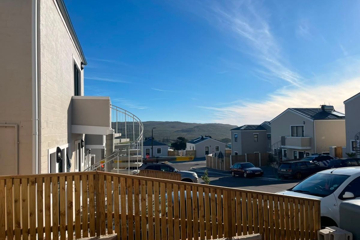 Exterior view of the apartment complex featuring a metal spiral staircase, timber fencing, and a retaining wall, overlooking the neighborhood and surrounding hills.