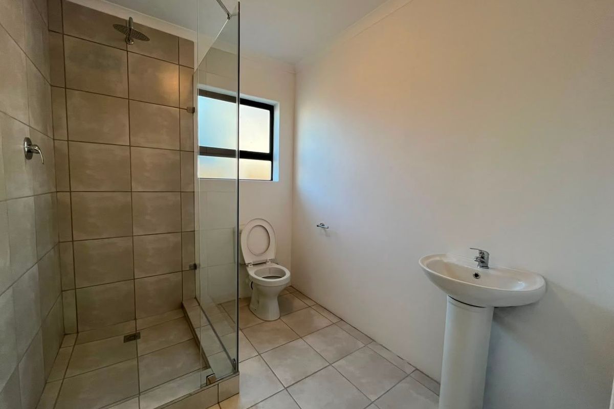 A clean, functional bathroom featuring a walk-in shower with glass screen, pedestal basin, and toilet with neutral tiled finishes.