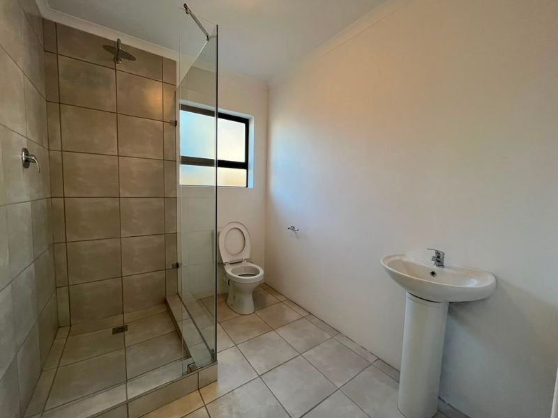 A clean, functional bathroom featuring a walk-in shower with glass screen, pedestal basin, and toilet with neutral tiled finishes.