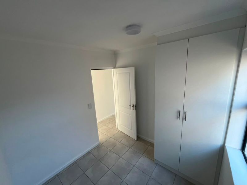 A clean, empty bedroom featuring neutral tiled flooring and a built-in wardrobe, offering a bright and versatile space ready for personalization.