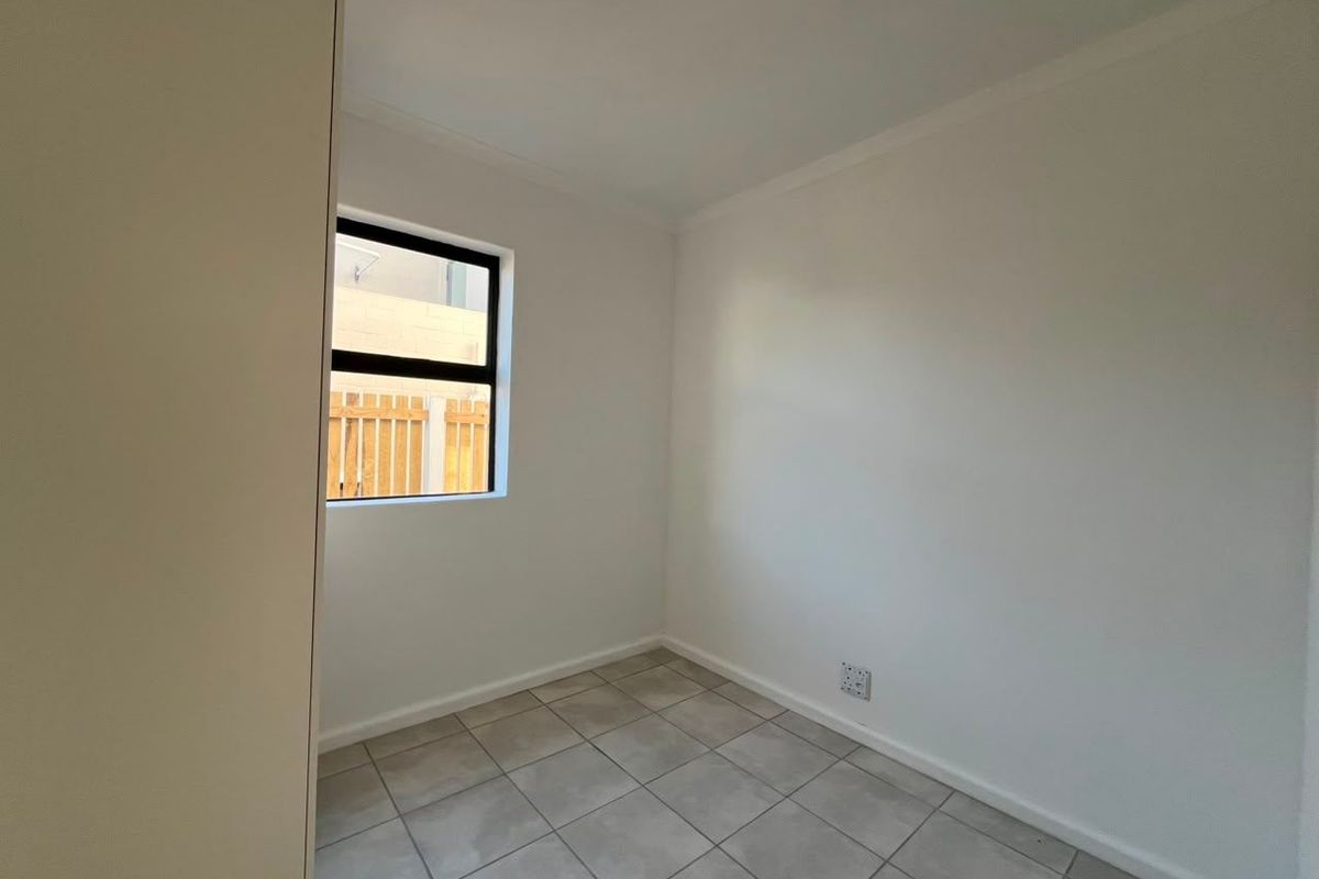 A clean, empty bedroom featuring neutral tiled flooring, a built-in cupboard, and a window with an aluminium frame.