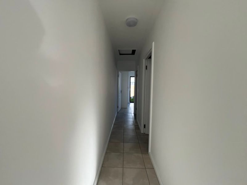 A clean, neutral hallway featuring tiled flooring and a ceiling access point, providing a simple transition between rooms in the apartment.