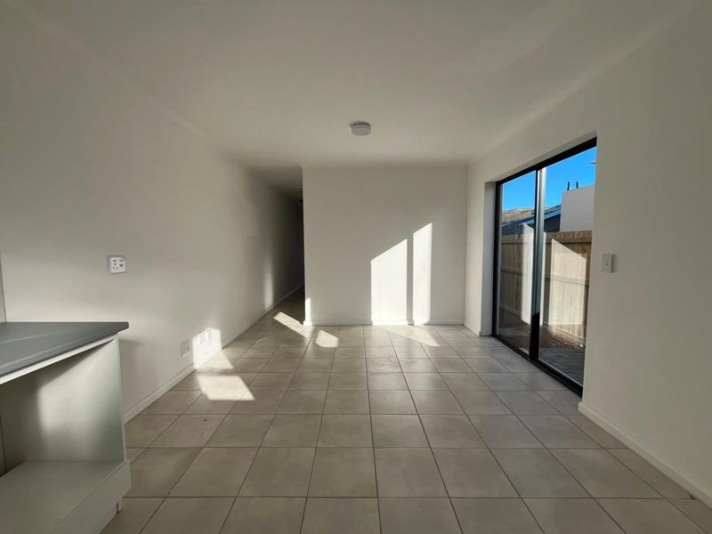 A bright, empty open-plan living area featuring neutral tiled flooring and a large sliding glass door providing access to the exterior.