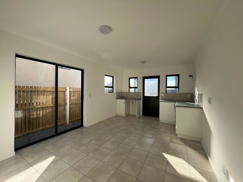 An open-plan kitchen and living area featuring tiled floors, neutral cabinetry, and a large sliding door providing access to the outdoor space.