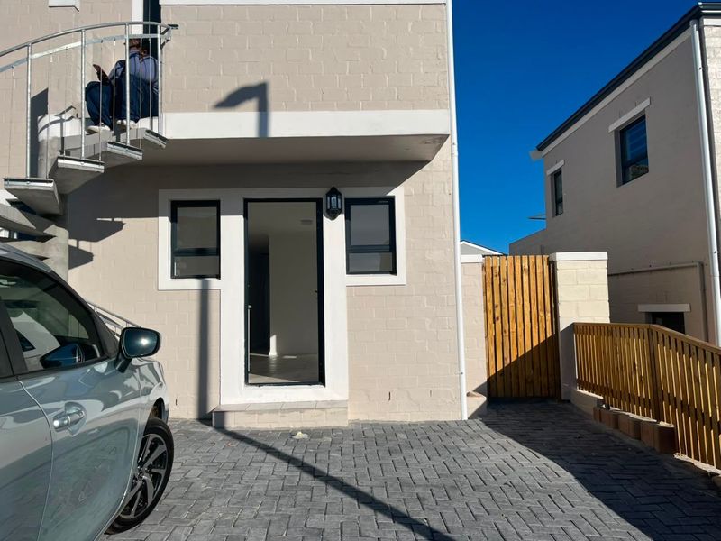 Front exterior view of the apartment featuring a paved driveway, timber fencing, and an external spiral staircase leading to the upper level.