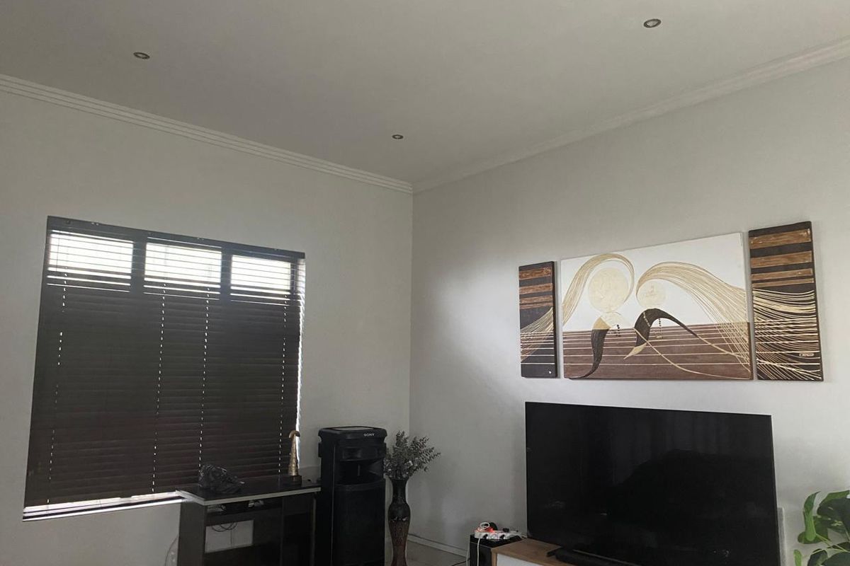 A well-lit living room featuring recessed downlighting, decorative coving, and dark venetian blinds, providing a neutral foundation for interior design.