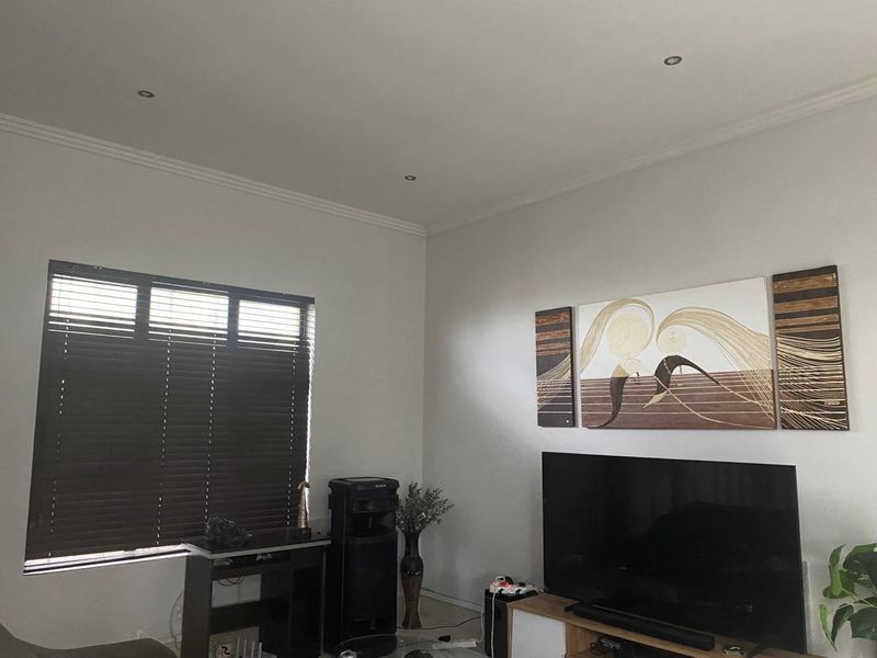 A well-lit living room featuring recessed downlighting, decorative coving, and dark venetian blinds, providing a neutral foundation for interior design.