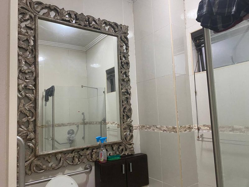 A functional bathroom featuring ceramic wall tiles, a glass shower enclosure, grab rails for accessibility, and a built-in vanity cabinet with a decorative mirror.