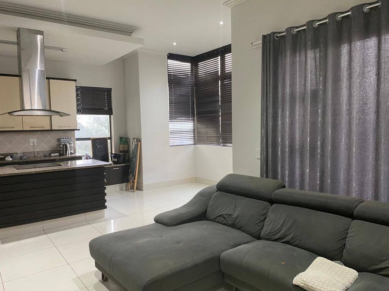 An open-plan living and kitchen area featuring modern cabinetry, granite countertops, a stainless steel extractor fan, and tiled flooring throughout.
