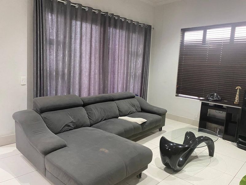 A living room featuring neutral tiled flooring, large window treatments with curtains, and venetian blinds, providing a functional and well-lit living space.