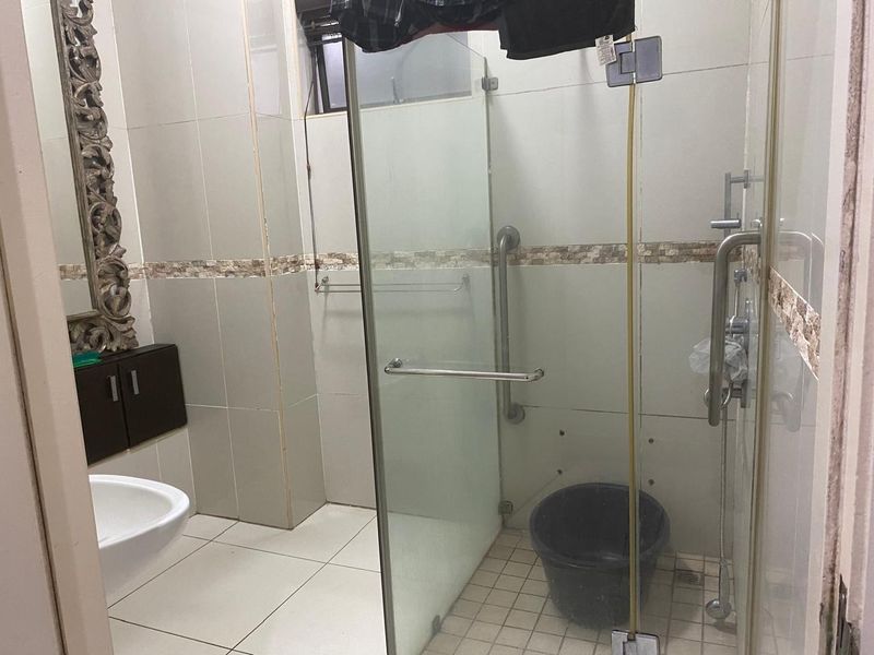 A bathroom featuring a glass-enclosed shower with grab rails, tiled finishes, and a wall-mounted vanity cabinet, requiring some maintenance and repair.