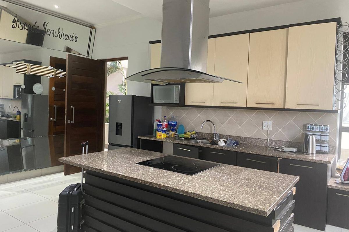 Modern kitchen featuring a central island with an electric hob, stone countertops, ample cabinetry, and a stainless steel extractor fan.