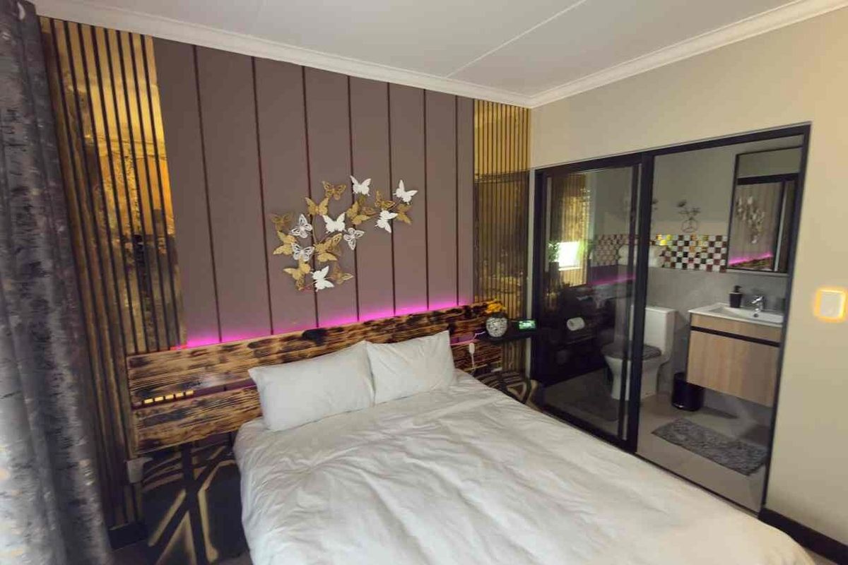 A modern bedroom featuring a custom headboard with integrated LED lighting and an en-suite bathroom separated by a sleek sliding glass door.