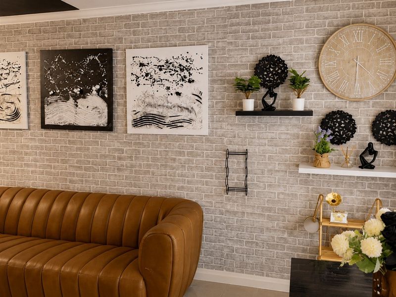 A well-maintained living room featuring a textured brick-effect feature wall, elegant crystal chandelier, and modern recessed ceiling lighting.