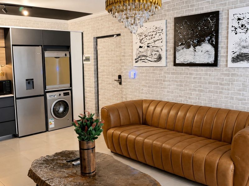 Modern open-plan living area featuring a sleek kitchen with integrated appliances, tiled flooring, and a distinctive brick-effect feature wall.