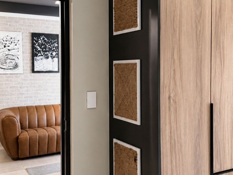 A modern hallway featuring sleek built-in cabinetry with wood-grain finish and black accents, leading into an adjacent living area.