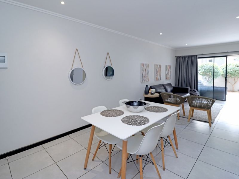 A bright open-plan living and dining area featuring neutral tiled flooring, recessed downlighting, and a sliding glass door leading to an outdoor space.