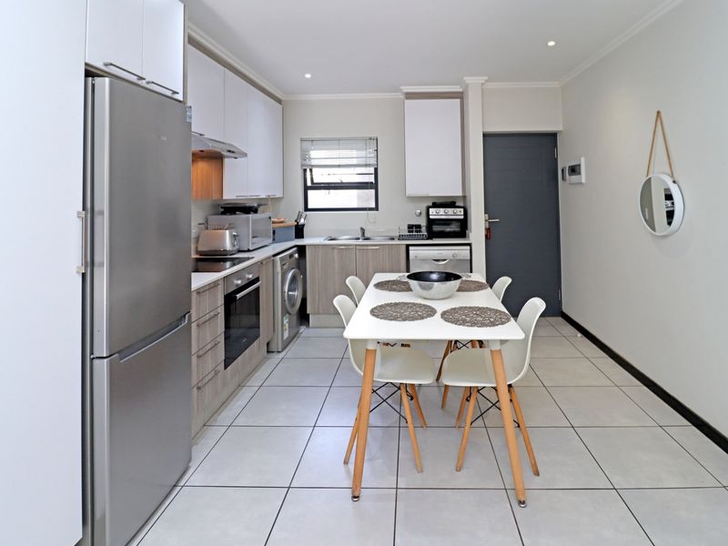 Modern open-plan kitchen and dining area featuring sleek cabinetry, integrated appliances, tiled flooring, and recessed lighting in a well-maintained apartment setting.