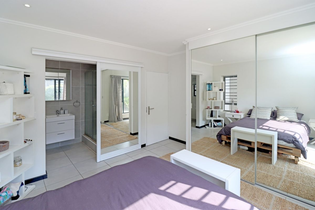 Spacious bedroom featuring tiled flooring, recessed lighting, a large mirrored built-in wardrobe, and an integrated en-suite bathroom with a modern vanity and shower.