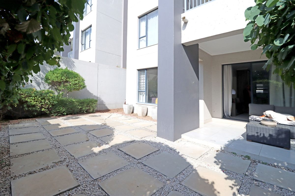 A private rear patio area featuring paved sections with gravel infill, accessible via sliding glass doors from the apartment interior.