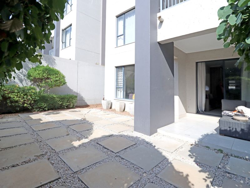 A private rear patio area featuring paved sections with gravel infill, accessible via sliding glass doors from the apartment interior.
