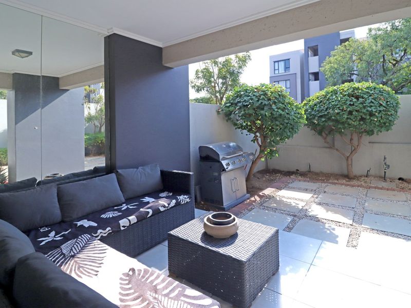 A covered patio area featuring tiled flooring, a mirrored wall panel, and a paved outdoor space with a boundary wall.