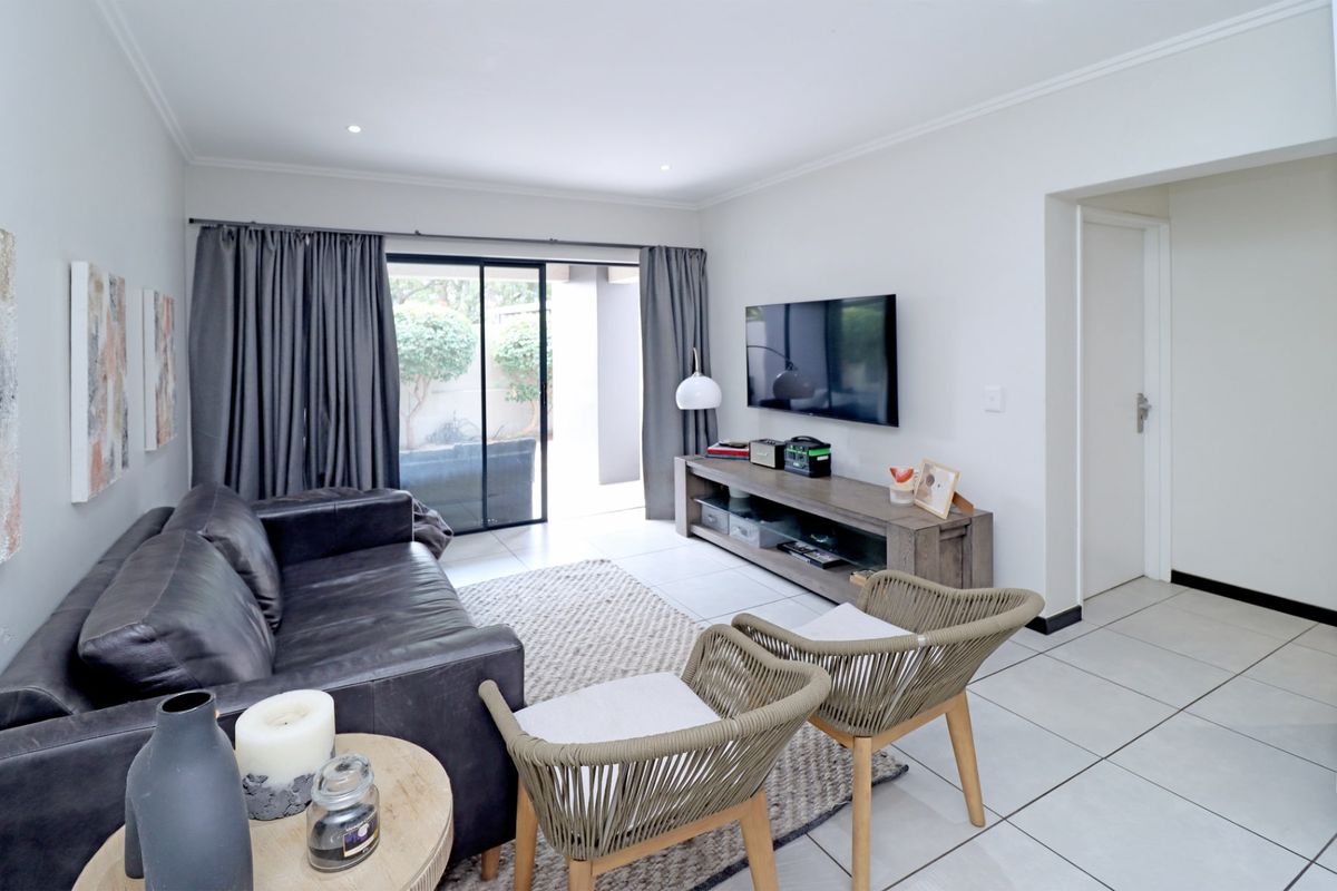 A bright and well-maintained living room featuring neutral tiled flooring, recessed lighting, and a large sliding glass door providing access to the patio.