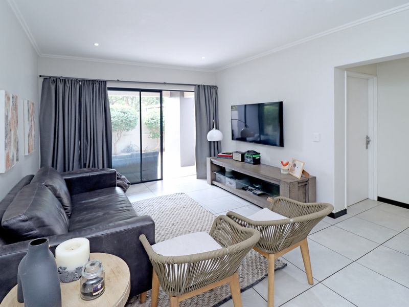 A bright and well-maintained living room featuring neutral tiled flooring, recessed lighting, and a large sliding glass door providing access to the patio.