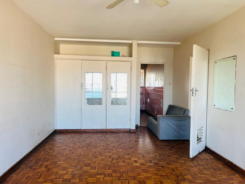 A bedroom featuring traditional parquet flooring, built-in cupboards with integrated mirrors, and a ceiling fan, offering a functional space with potential for modernization.