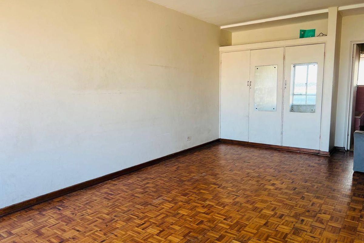 An empty bedroom featuring traditional parquet flooring and built-in storage cupboards, presenting a blank canvas for renovation or interior design updates.