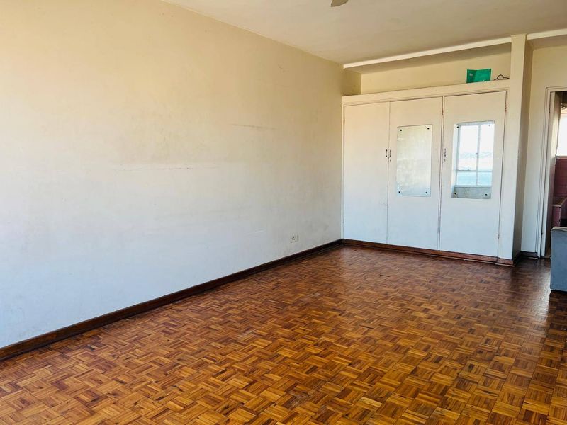 An empty bedroom featuring traditional parquet flooring and built-in storage cupboards, presenting a blank canvas for renovation or interior design updates.