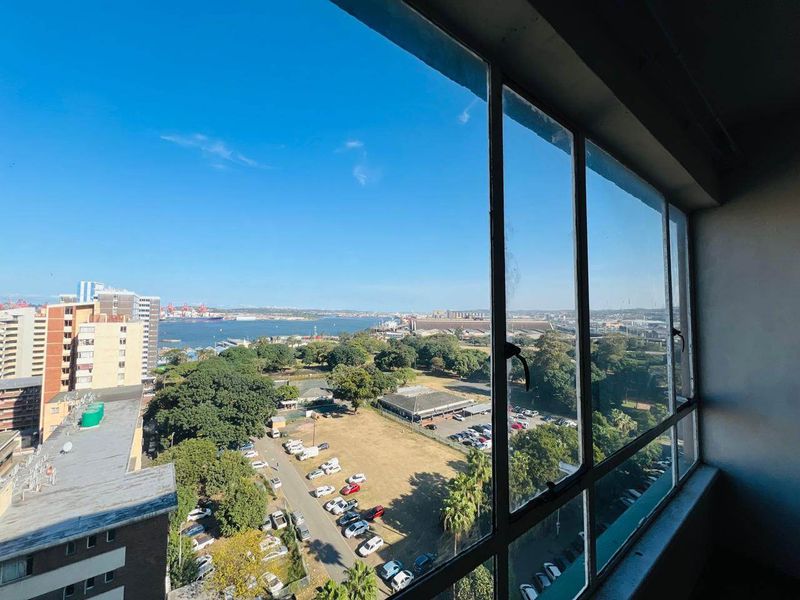 Elevated urban and harbour view captured through large steel-framed windows, showcasing the surrounding cityscape and coastal landscape.
