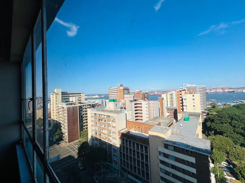 An elevated city and harbour view captured through a large window, showcasing the surrounding urban landscape and coastal proximity.