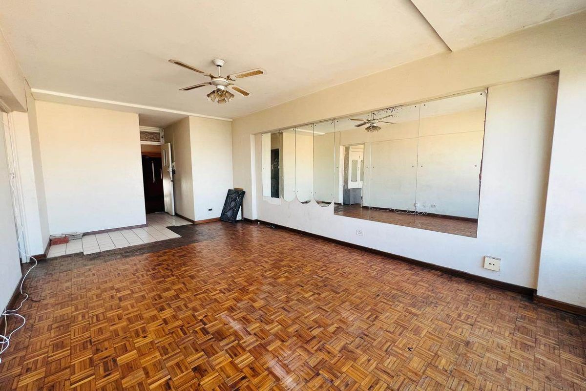 Spacious living area featuring original parquet flooring, a ceiling fan, and a large wall-mounted mirror panel, offering a blank canvas for renovation.