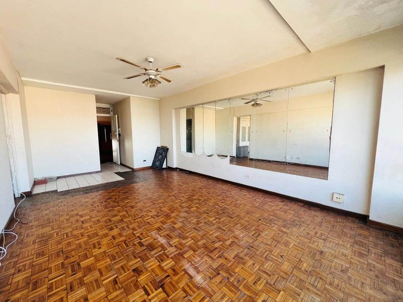 Spacious living area featuring original parquet flooring, a ceiling fan, and a large wall-mounted mirror panel, offering a blank canvas for renovation.