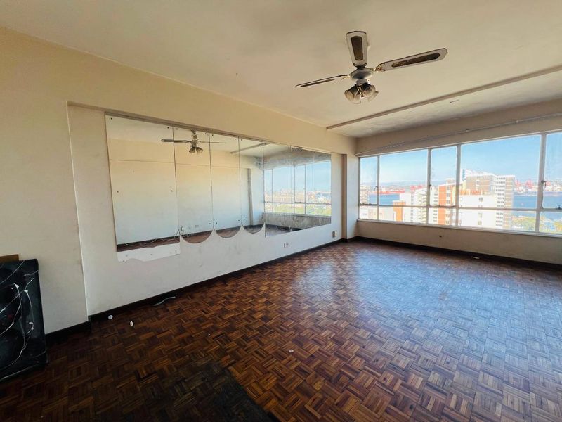 Spacious living area featuring original parquet flooring, a ceiling fan, and large windows offering expansive city and harbor views.