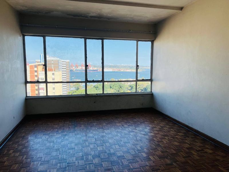 Empty living area featuring original parquet flooring and large windows with expansive harbour and city views, requiring cosmetic refurbishment.