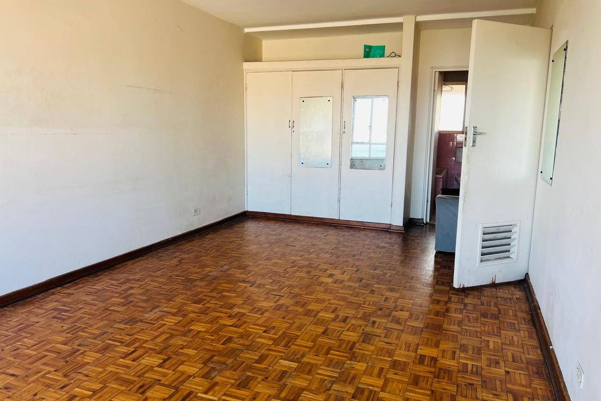 An empty bedroom featuring original parquet flooring and built-in cupboards, requiring cosmetic updates to restore its appeal.